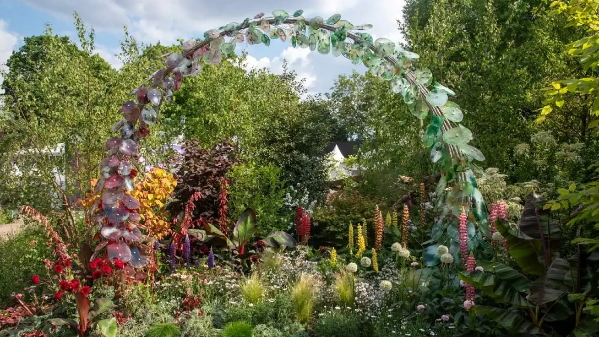 A vibrant feature garden showcases a large rainbow-coloured arch, surrounded by lush, eclectic planting with red, yellow, and purple blooms.