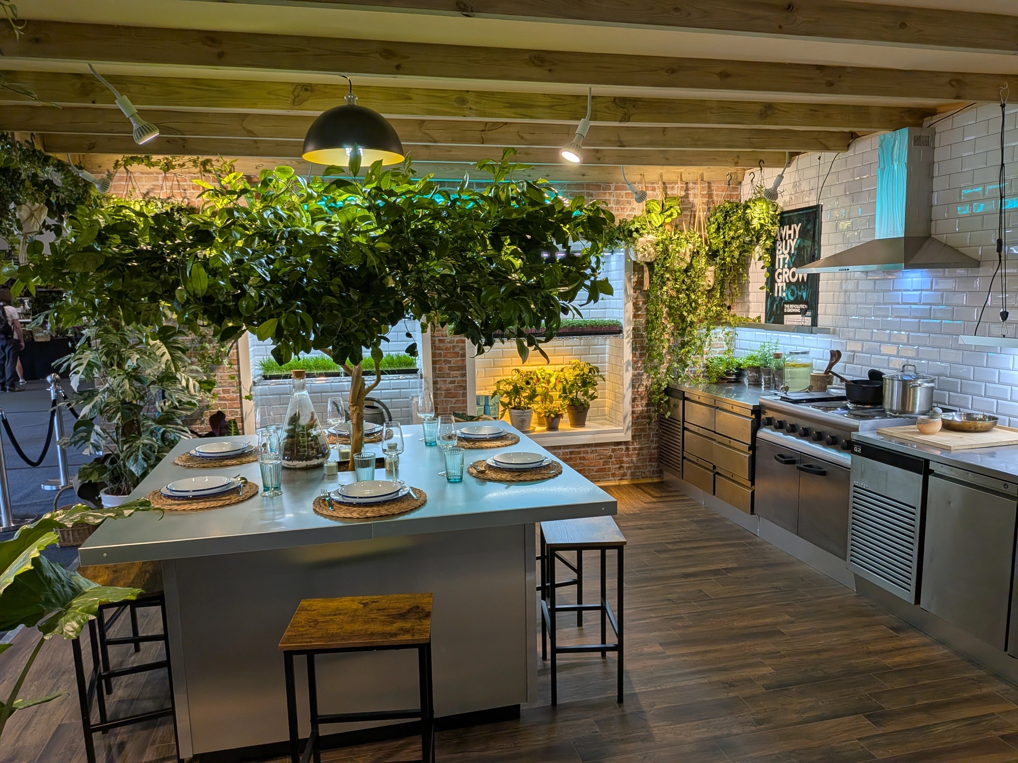 A modern indoor kitchen garden showcases a large island with a citrus tree, surrounded by edible plants, and illuminated by grow lights.